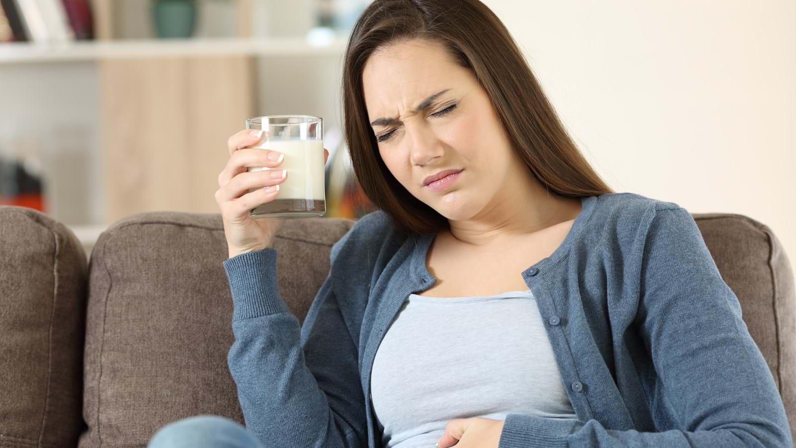Kvinne som ser ut til å ha magesmerter mens hun holder et glass melk.