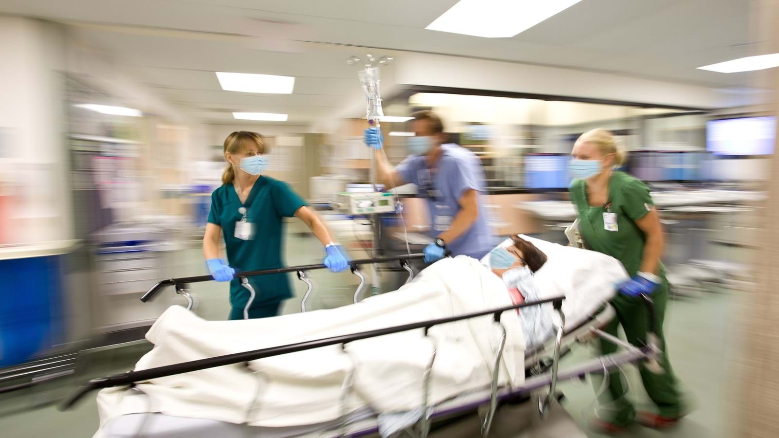 Medisinsk personell som ruller en pasient på en båre gjennom en sykehuskorridor.